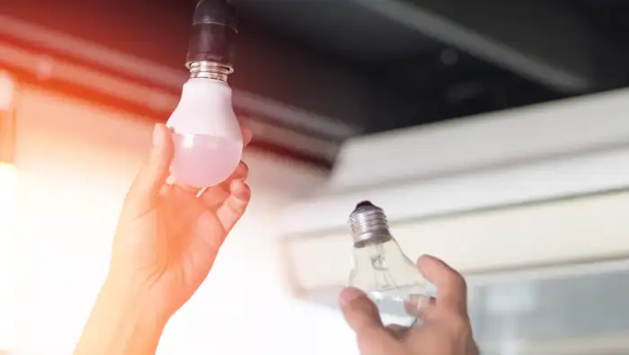 Zwei Hände, die eine Glühbirne ersetzen und eine LED-Birne einschrauben.